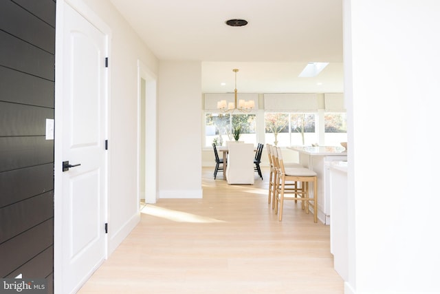 hallway featuring a skylight, an inviting chandelier, and light hardwood / wood-style floors