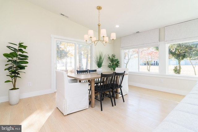 dining space with light wood-type flooring, a healthy amount of sunlight, vaulted ceiling, and an inviting chandelier