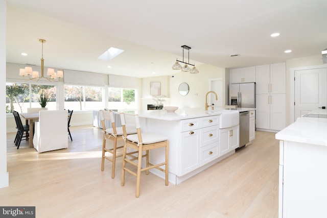 kitchen featuring stainless steel appliances, white cabinetry, hanging light fixtures, sink, and a kitchen island with sink