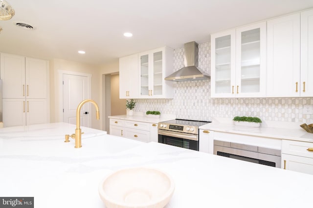 kitchen with stainless steel appliances, wall chimney range hood, white cabinets, and backsplash