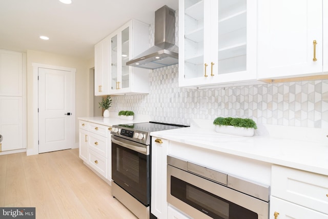 kitchen featuring white cabinets, stainless steel appliances, light hardwood / wood-style floors, and wall chimney range hood