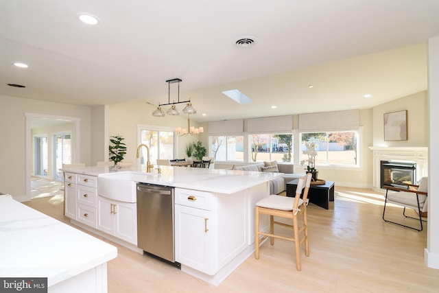 kitchen featuring white cabinetry, decorative light fixtures, an island with sink, light hardwood / wood-style floors, and stainless steel dishwasher