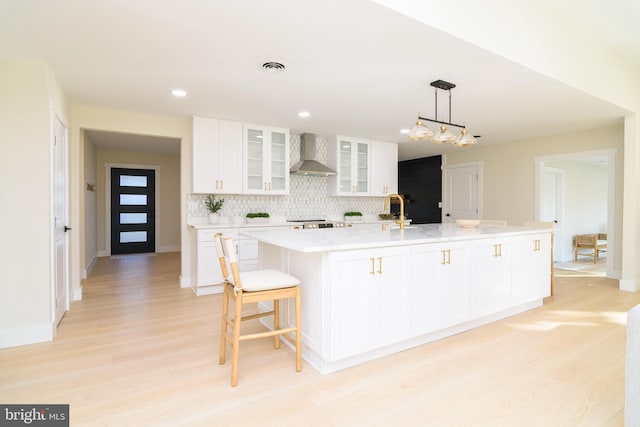 kitchen featuring an island with sink, white cabinetry, wall chimney exhaust hood, and light hardwood / wood-style flooring