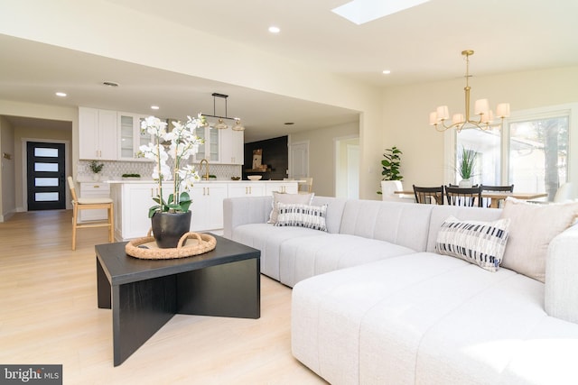 living room featuring an inviting chandelier, light wood-type flooring, a skylight, and sink