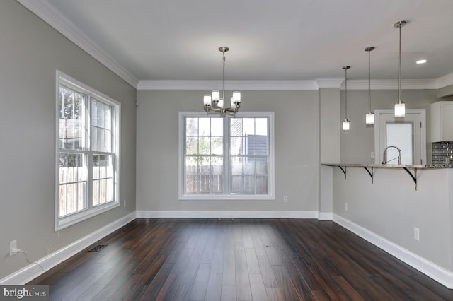 unfurnished dining area featuring dark wood-type flooring, an inviting chandelier, and ornamental molding