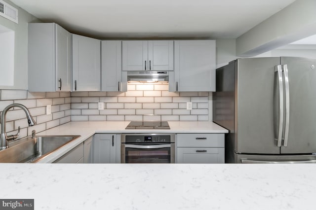 kitchen featuring appliances with stainless steel finishes, gray cabinets, light stone countertops, sink, and decorative backsplash