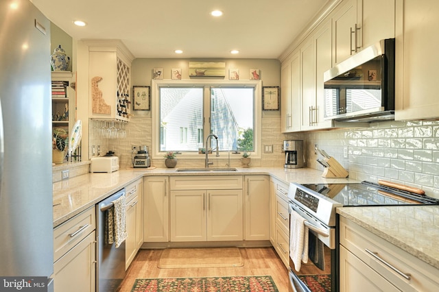 kitchen featuring sink, light stone counters, appliances with stainless steel finishes, backsplash, and light hardwood / wood-style flooring