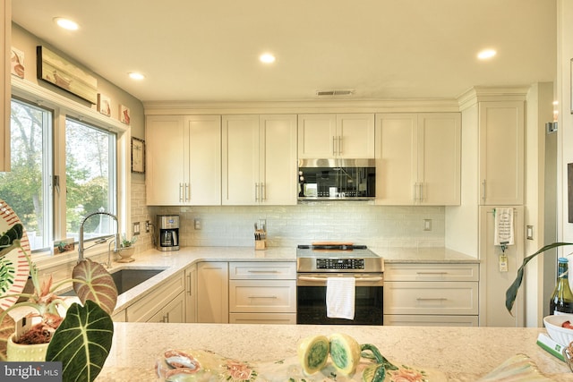 kitchen with stainless steel appliances, sink, backsplash, and light stone counters