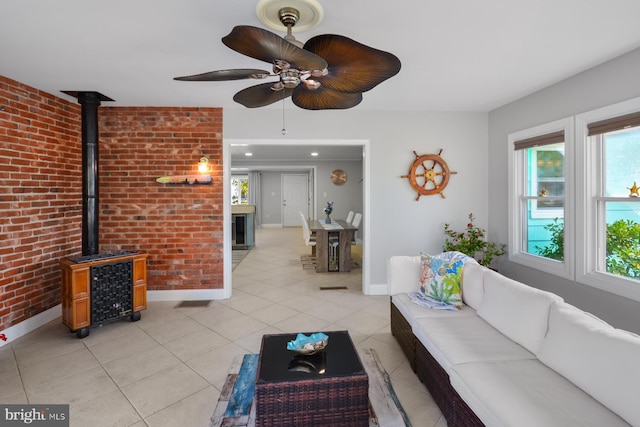 unfurnished living room with brick wall, a wood stove, light tile patterned floors, and ceiling fan