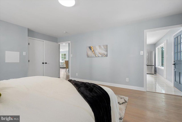 bedroom featuring stainless steel fridge, multiple windows, a closet, and light wood-type flooring