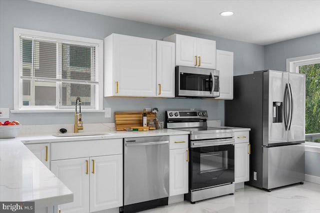 kitchen with white cabinets, appliances with stainless steel finishes, sink, and light stone countertops