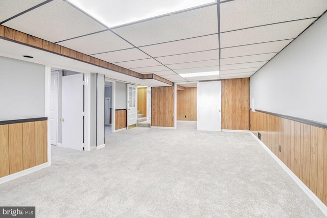 basement with a paneled ceiling, wood walls, and light colored carpet