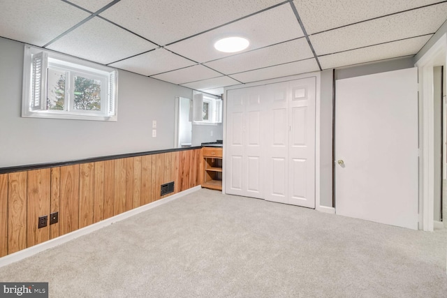 basement featuring carpet flooring, a paneled ceiling, and wooden walls