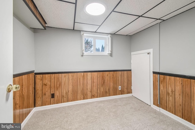 basement with a paneled ceiling, light carpet, and wood walls