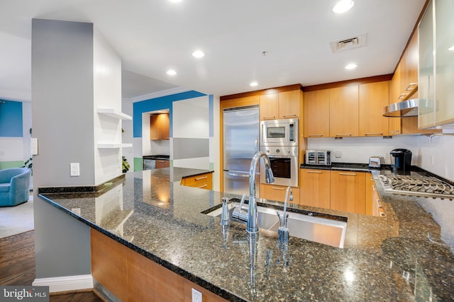 kitchen with kitchen peninsula, dark stone countertops, built in appliances, and ornamental molding