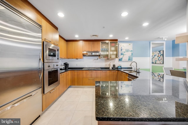 kitchen with light tile patterned floors, sink, dark stone countertops, and built in appliances