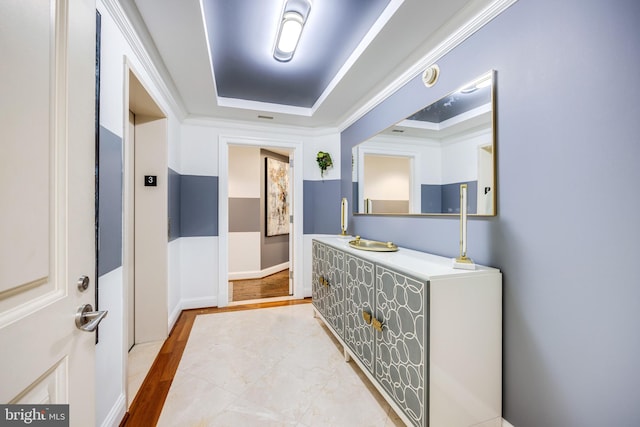 corridor with a tray ceiling, crown molding, and light wood-type flooring