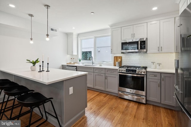 kitchen featuring appliances with stainless steel finishes, decorative light fixtures, gray cabinets, sink, and light hardwood / wood-style floors