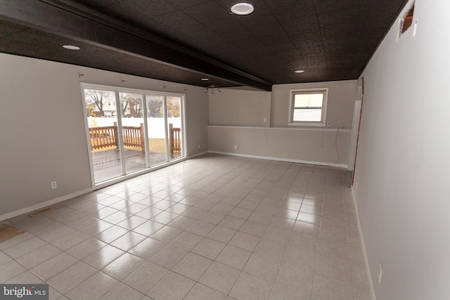 empty room with beamed ceiling, light tile patterned floors, and a healthy amount of sunlight