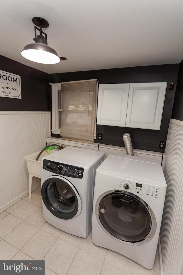 clothes washing area featuring washer and dryer, light tile patterned floors, and cabinets