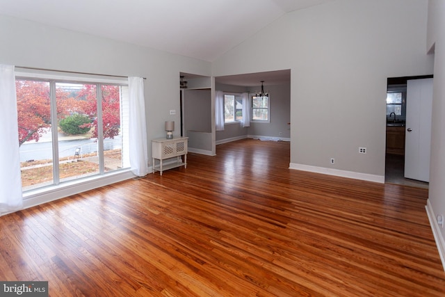 unfurnished living room with sink, an inviting chandelier, high vaulted ceiling, and hardwood / wood-style flooring