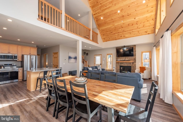 dining room featuring high vaulted ceiling, a stone fireplace, and hardwood / wood-style floors