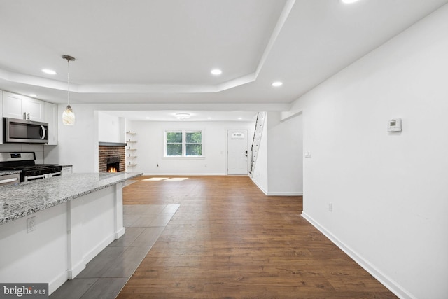 kitchen featuring stainless steel appliances, dark wood-type flooring, white cabinets, light stone countertops, and decorative light fixtures