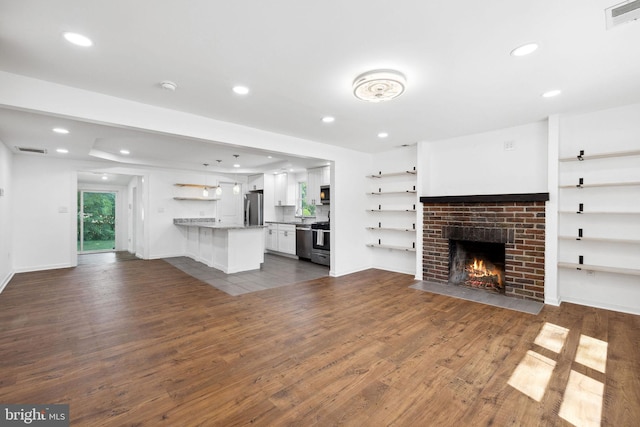 unfurnished living room with dark wood-type flooring and a brick fireplace