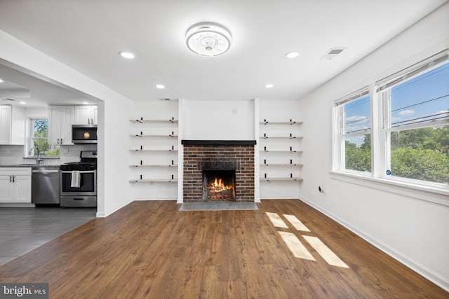 unfurnished living room featuring sink, dark hardwood / wood-style floors, and a brick fireplace