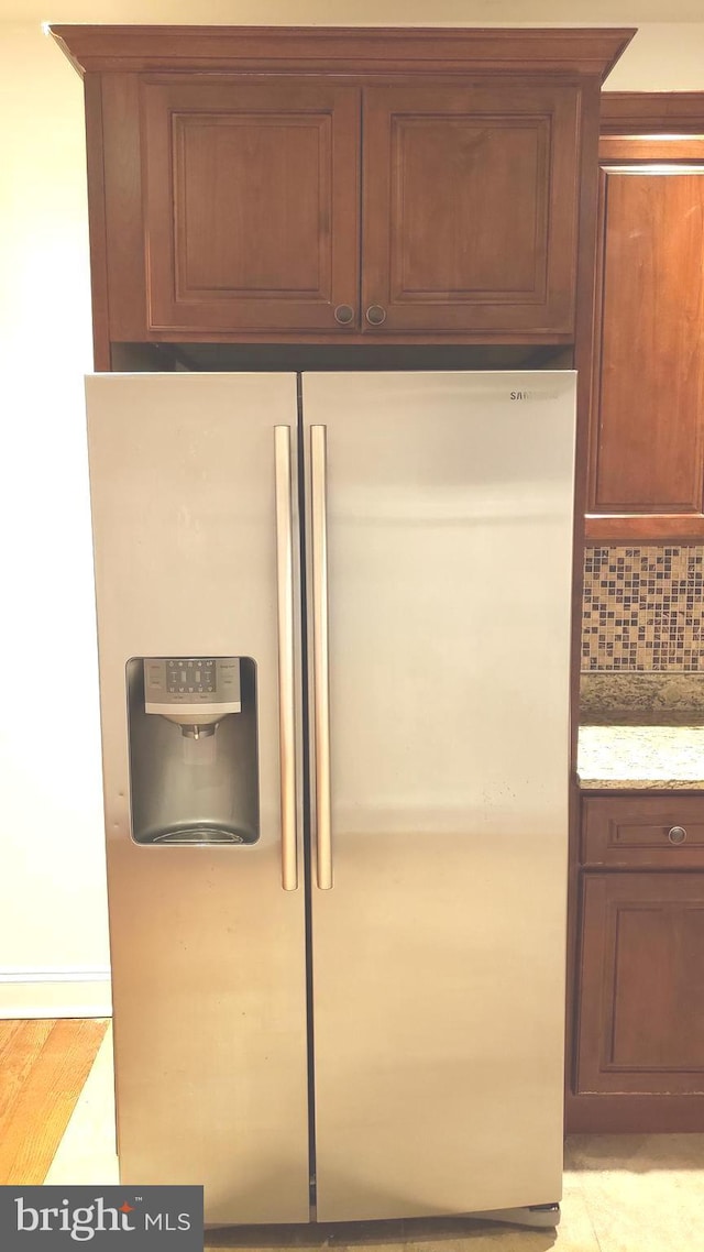 interior details with decorative backsplash, stainless steel fridge, light stone counters, and light wood-type flooring