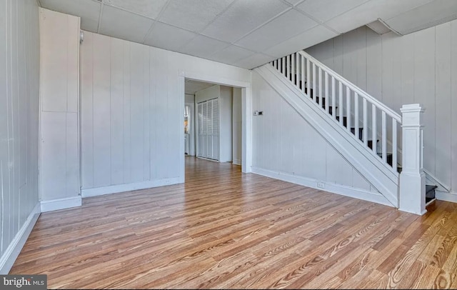 interior space with a drop ceiling, light wood-type flooring, and wooden walls