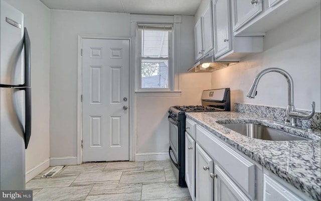 kitchen featuring light stone countertops, black gas stove, sink, and stainless steel fridge