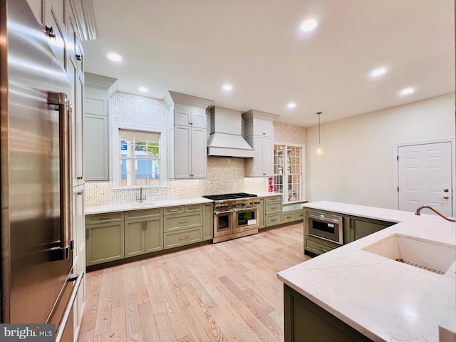 kitchen with premium range hood, pendant lighting, high quality appliances, green cabinetry, and sink