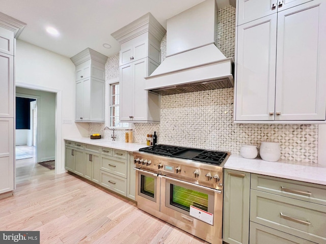 kitchen featuring light stone counters, light hardwood / wood-style floors, tasteful backsplash, custom exhaust hood, and range with two ovens