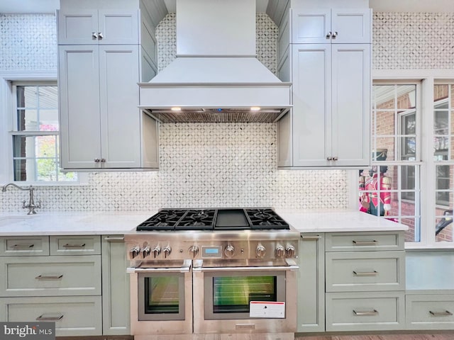 kitchen with light stone countertops, premium range hood, range with two ovens, sink, and tasteful backsplash