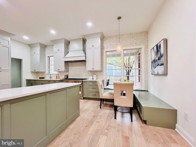 kitchen featuring custom exhaust hood, decorative light fixtures, green cabinetry, decorative backsplash, and light wood-type flooring