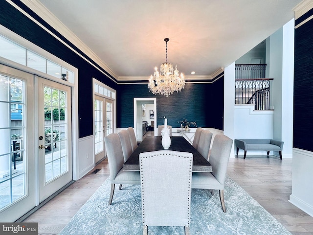 dining area with ornamental molding, light wood-type flooring, french doors, and a chandelier