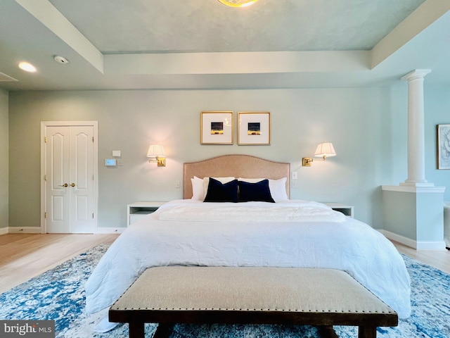 bedroom featuring ornate columns, a tray ceiling, and wood-type flooring