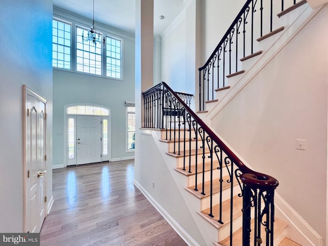 entryway with ornamental molding, a towering ceiling, a chandelier, and hardwood / wood-style flooring