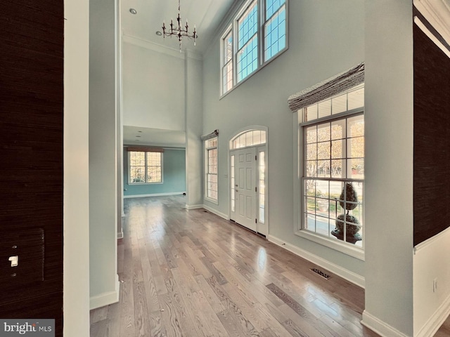 entrance foyer with light hardwood / wood-style floors, a towering ceiling, crown molding, and a chandelier