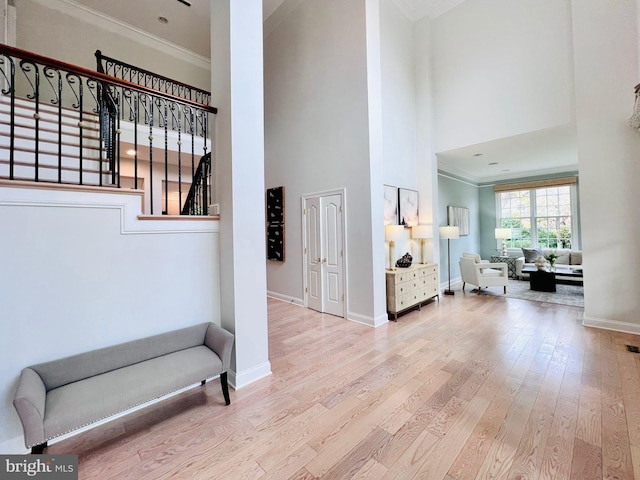 hallway with a towering ceiling, crown molding, and light hardwood / wood-style flooring