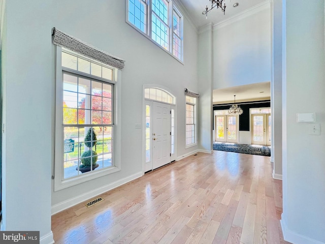 foyer entrance with light hardwood / wood-style floors, ornamental molding, a towering ceiling, and a chandelier