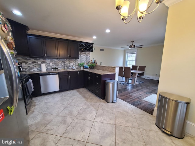 kitchen with kitchen peninsula, appliances with stainless steel finishes, ornamental molding, ceiling fan with notable chandelier, and decorative light fixtures