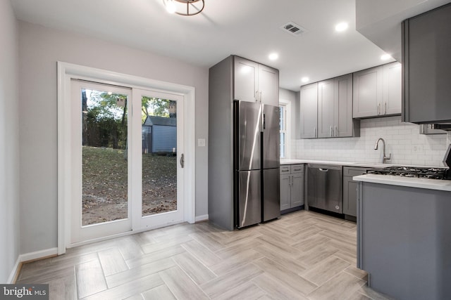 kitchen featuring light parquet flooring, gray cabinetry, tasteful backsplash, stainless steel appliances, and sink