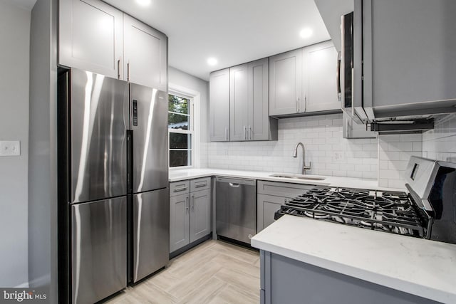 kitchen featuring appliances with stainless steel finishes, sink, backsplash, and gray cabinetry