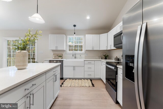 kitchen with pendant lighting, white cabinets, a sink, stainless steel appliances, and light wood finished floors