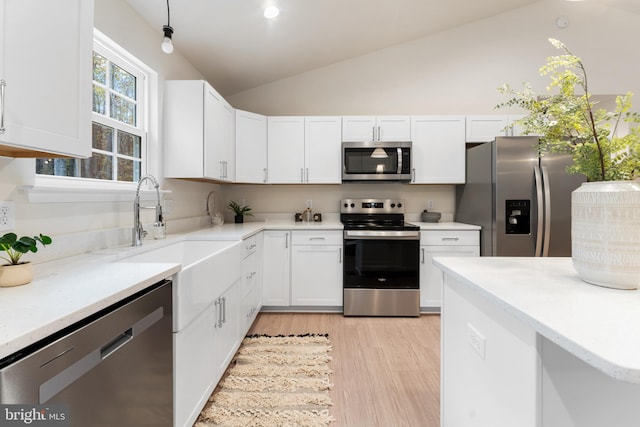 kitchen featuring light wood-type flooring, white cabinets, appliances with stainless steel finishes, a sink, and lofted ceiling