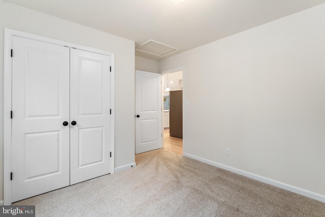 unfurnished bedroom with light carpet, attic access, baseboards, and a closet