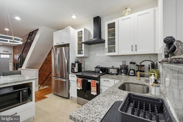 kitchen with light stone counters, wall chimney exhaust hood, light tile patterned floors, white cabinetry, and appliances with stainless steel finishes