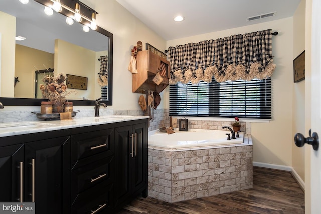 bathroom featuring vanity, a relaxing tiled tub, and wood-type flooring